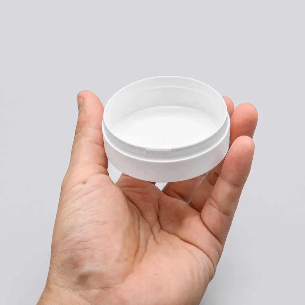 Hand holding a closed white flip-top snus can, top view