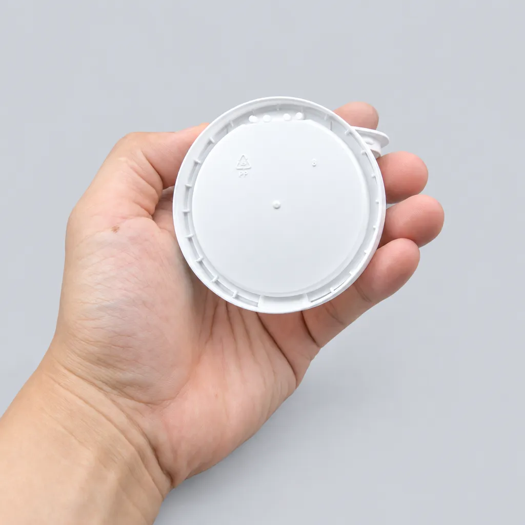 Bottom view of a white flip-top snus can in hand with PP recycling mark