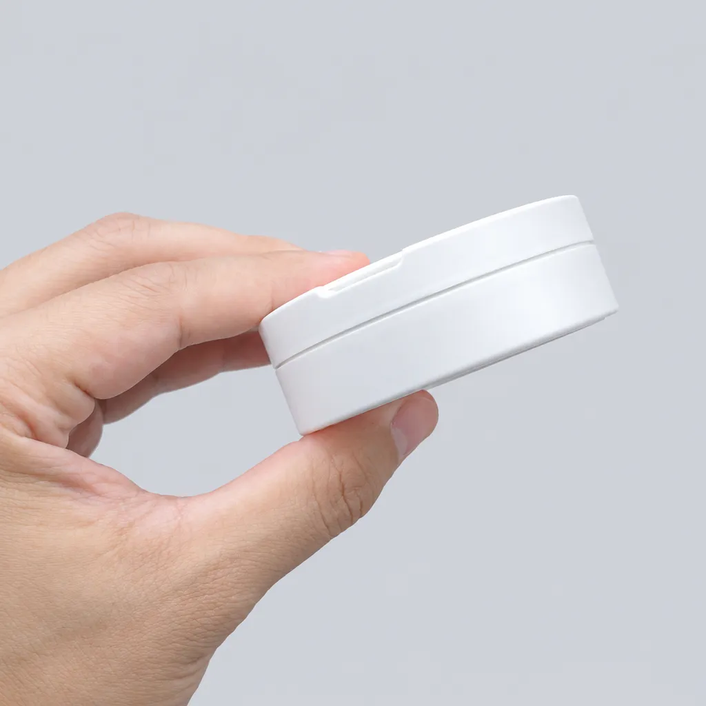 Closed white flip-top snus can held between two fingers, slim side profile