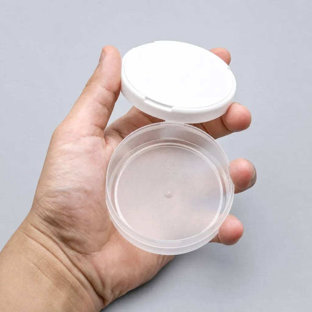 Hand holding a translucent snus can with the white snap-on lid open, showing its structure