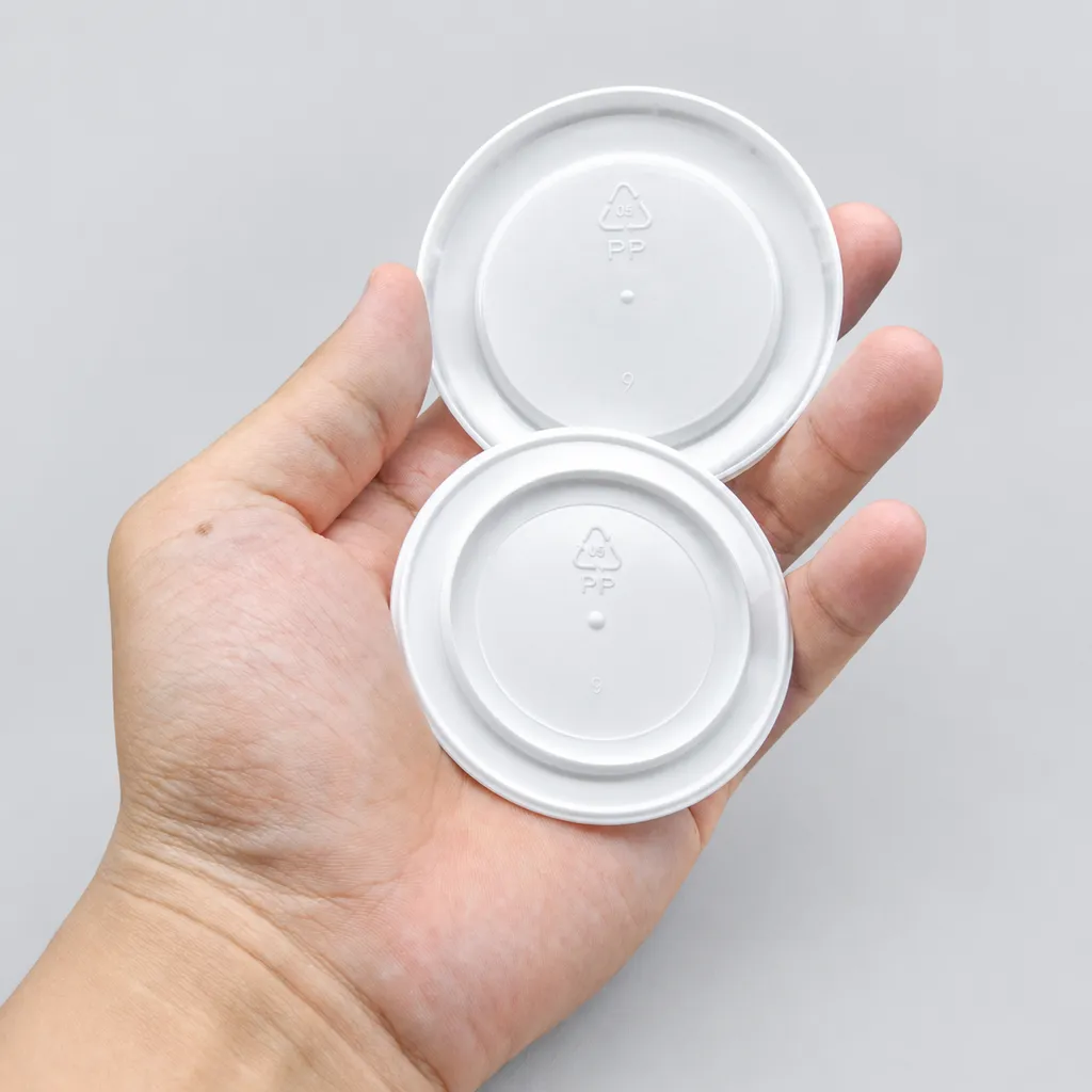Hand holding two white snap-on lids with PP recycling marks